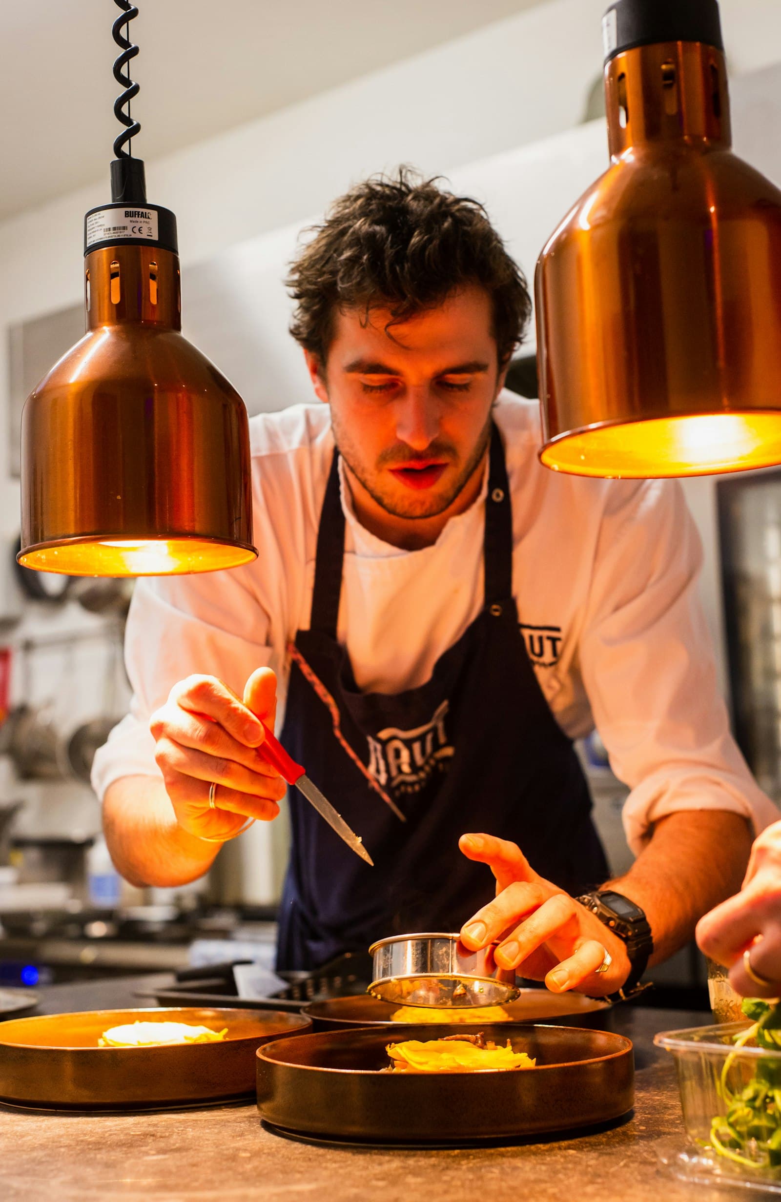 A chef plating food at the pass in a busy restaurant kitchen